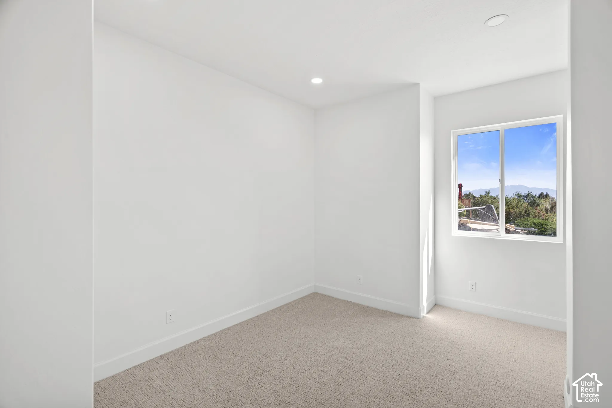 Recessed ceiling lighting, white painted walls, light-toned carpeting, white window frame, and a clear sky outside