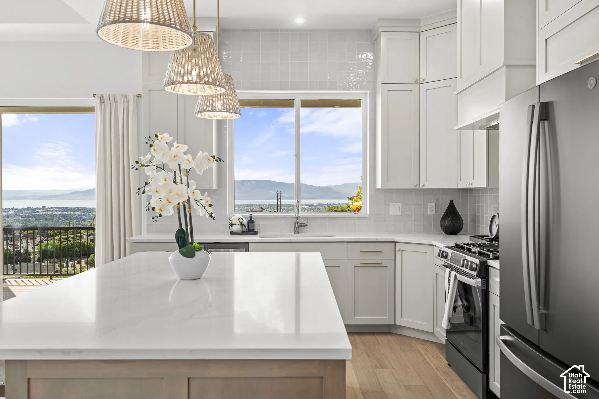 Kitchen featuring a peninsula island with a light-toned countertop, white cabinetry with gold-finish hardware, stainless steel appliances, and wood-finish flooring
