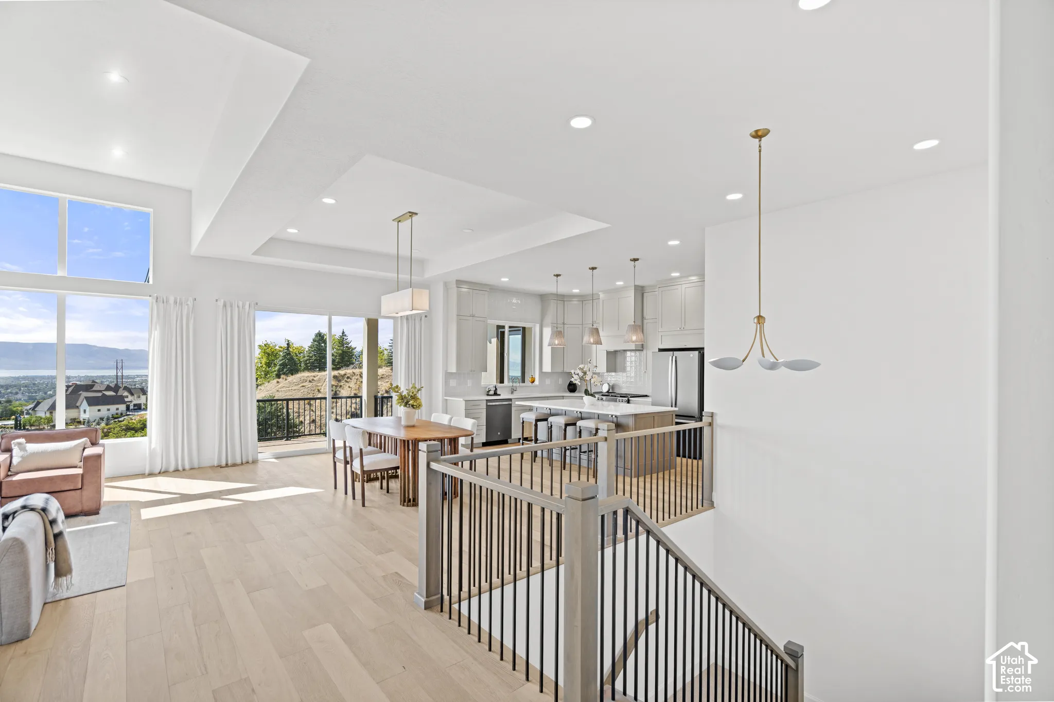 Open-concept living space featuring high ceilings, wood-finish flooring, a kitchen island with seating, pendant lighting, and a staircase with metal railings