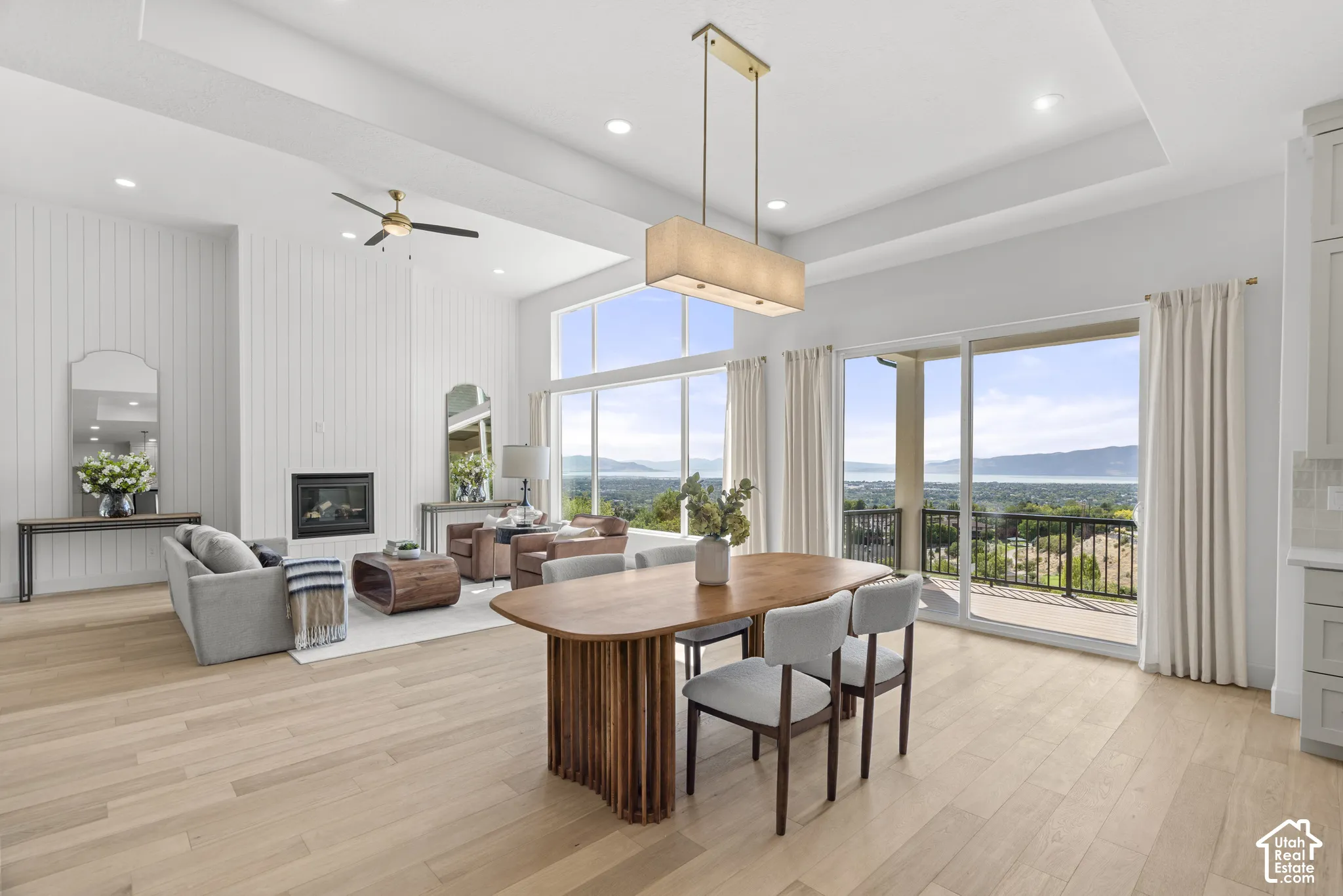 Spacious open-concept living area featuring light wood-finish flooring, a contemporary fireplace with white vertical paneling, and a white tray ceiling