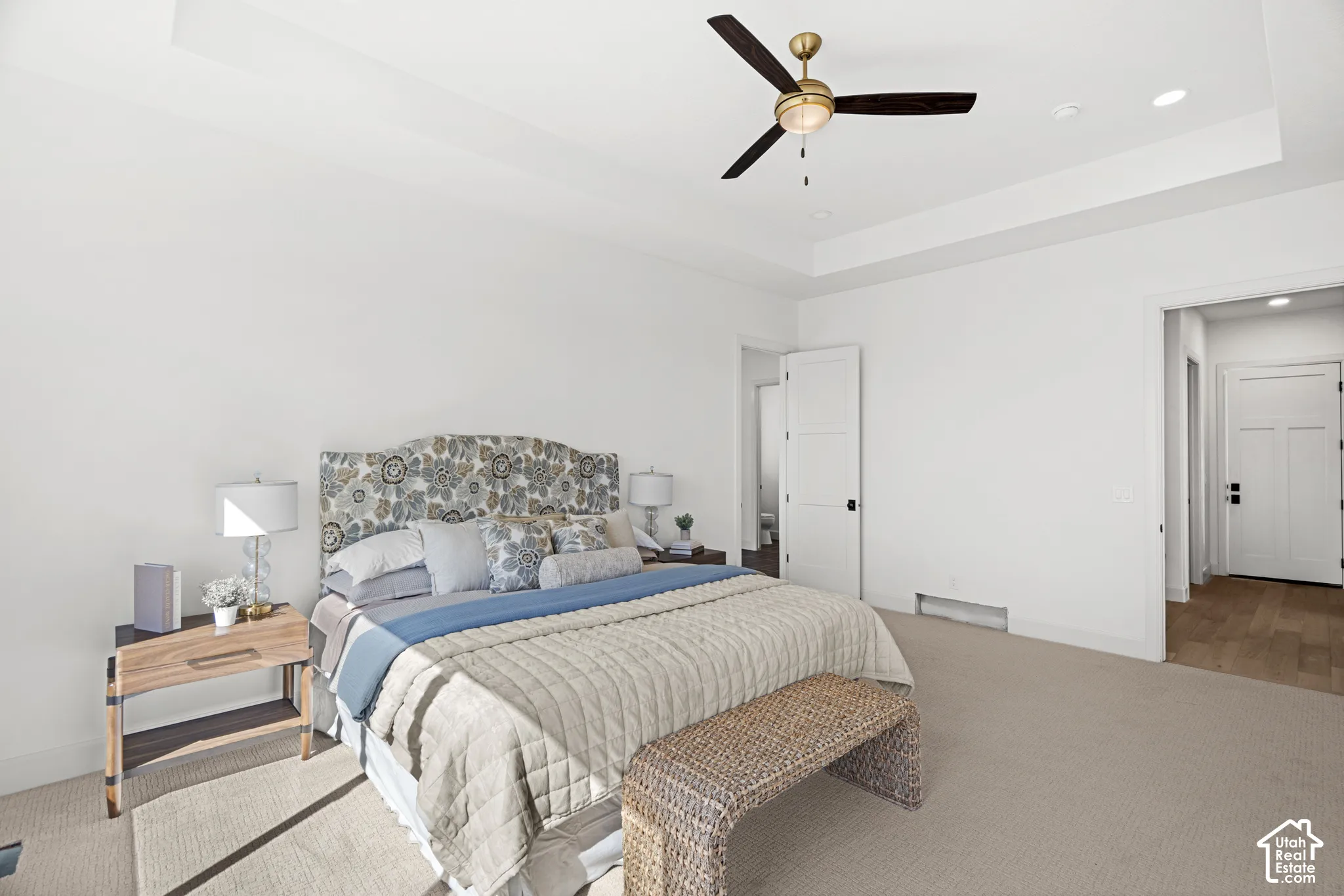 Tray ceiling with recessed lighting, ceiling fan with integrated light, light-toned carpeting, white interior doors, and wood-finish flooring visible through doorway