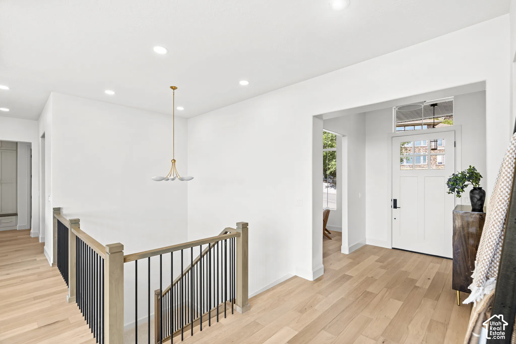 Hardwood flooring throughout, recessed lighting, modern chandelier, craftsman-style entry door with transom window, and staircase with wood newel posts and black metal balusters