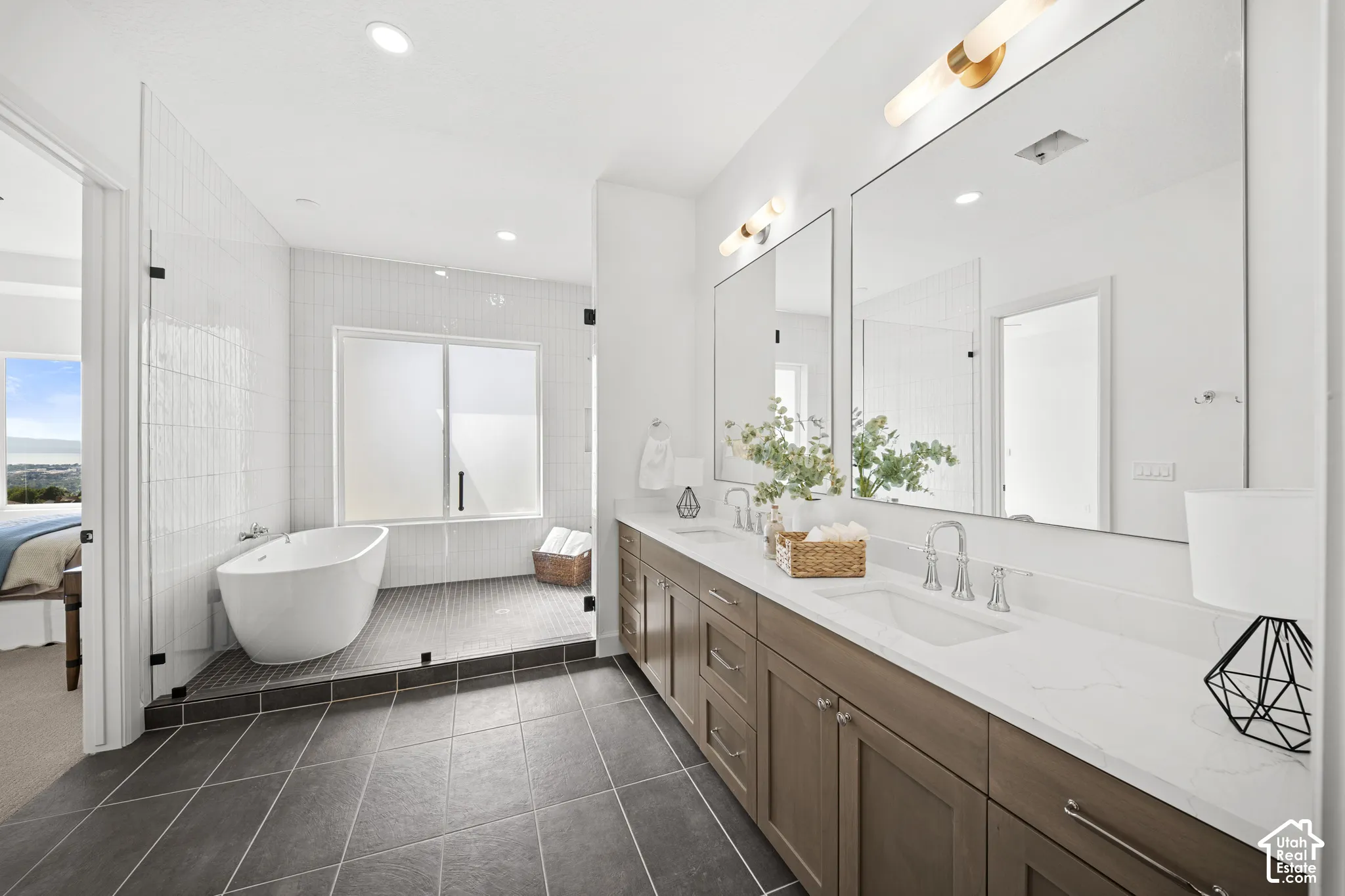 Spacious bathroom featuring a freestanding soaking tub, dual vanity with undermount sinks, stone countertops, and a glass-enclosed shower with tile surround