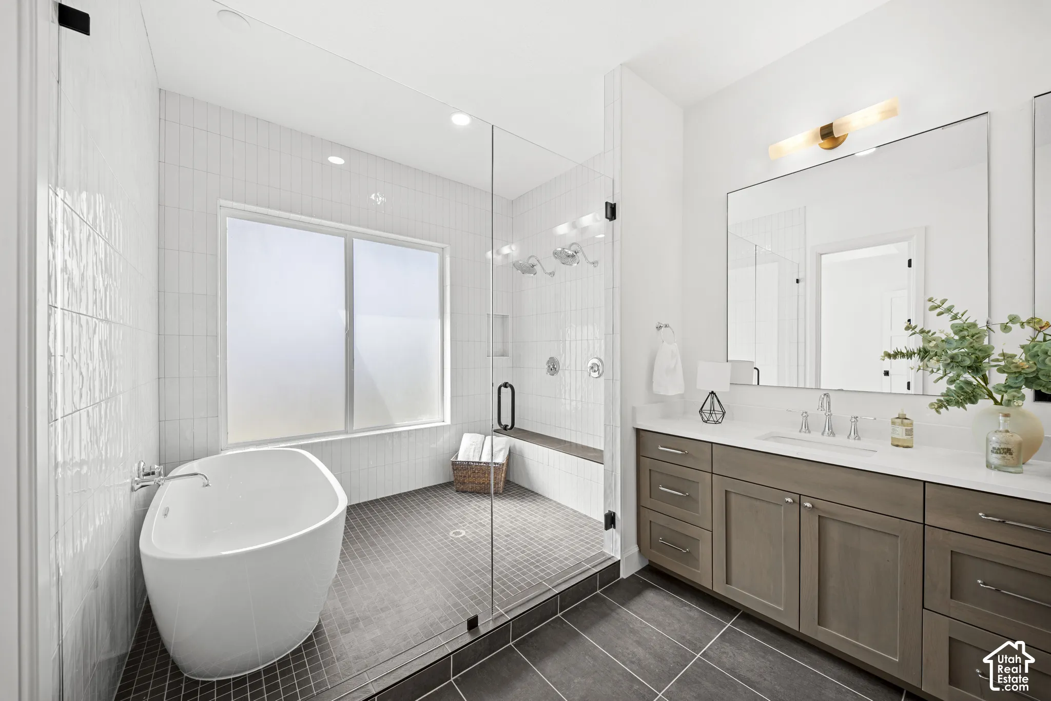 Freestanding soaking tub, glass-enclosed shower with integrated bench, dual vanity with undermount sink, quartz countertop, and large framed mirror