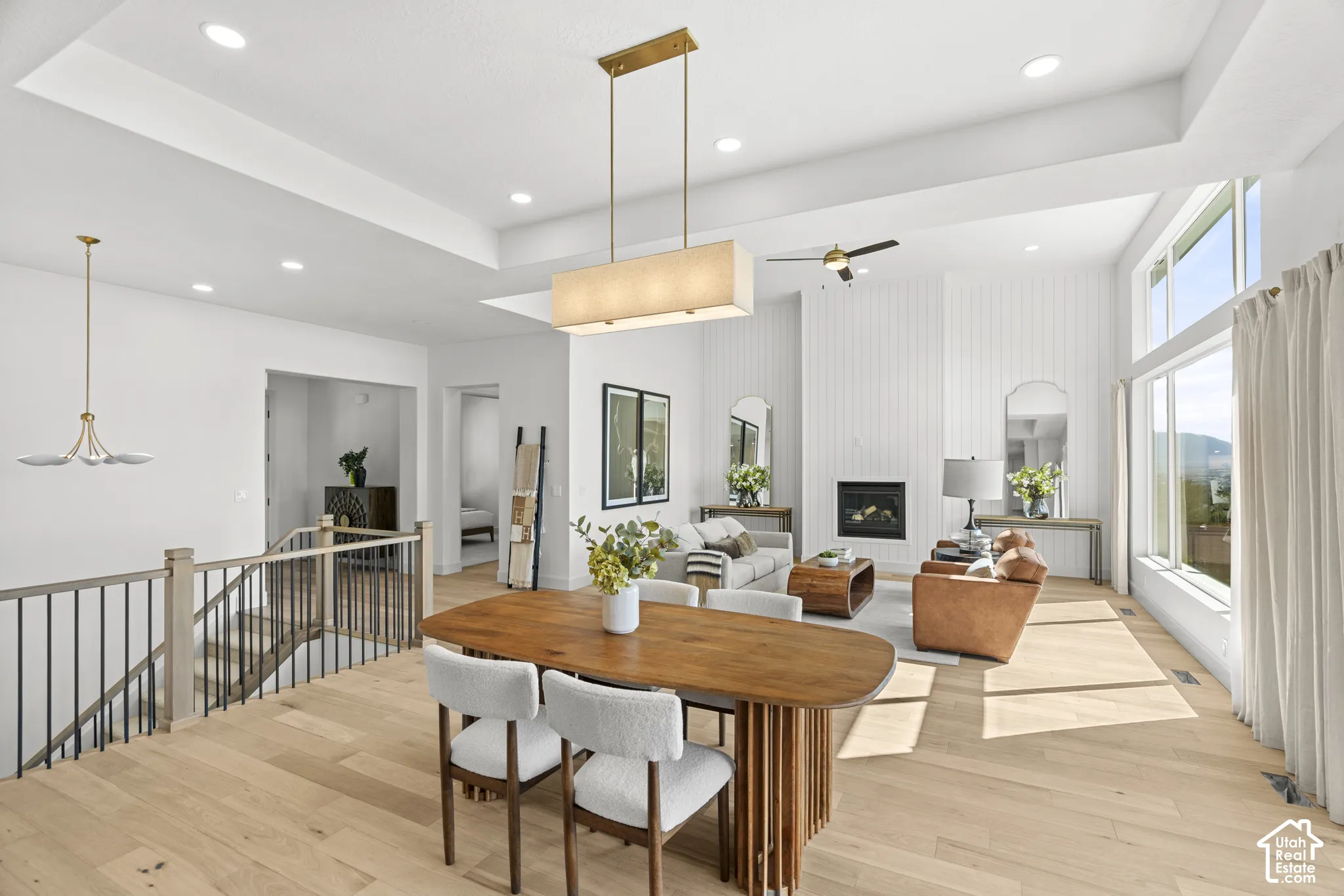 Open-concept living area with wood-finish flooring, a contemporary fireplace, tray ceilings, and large windows