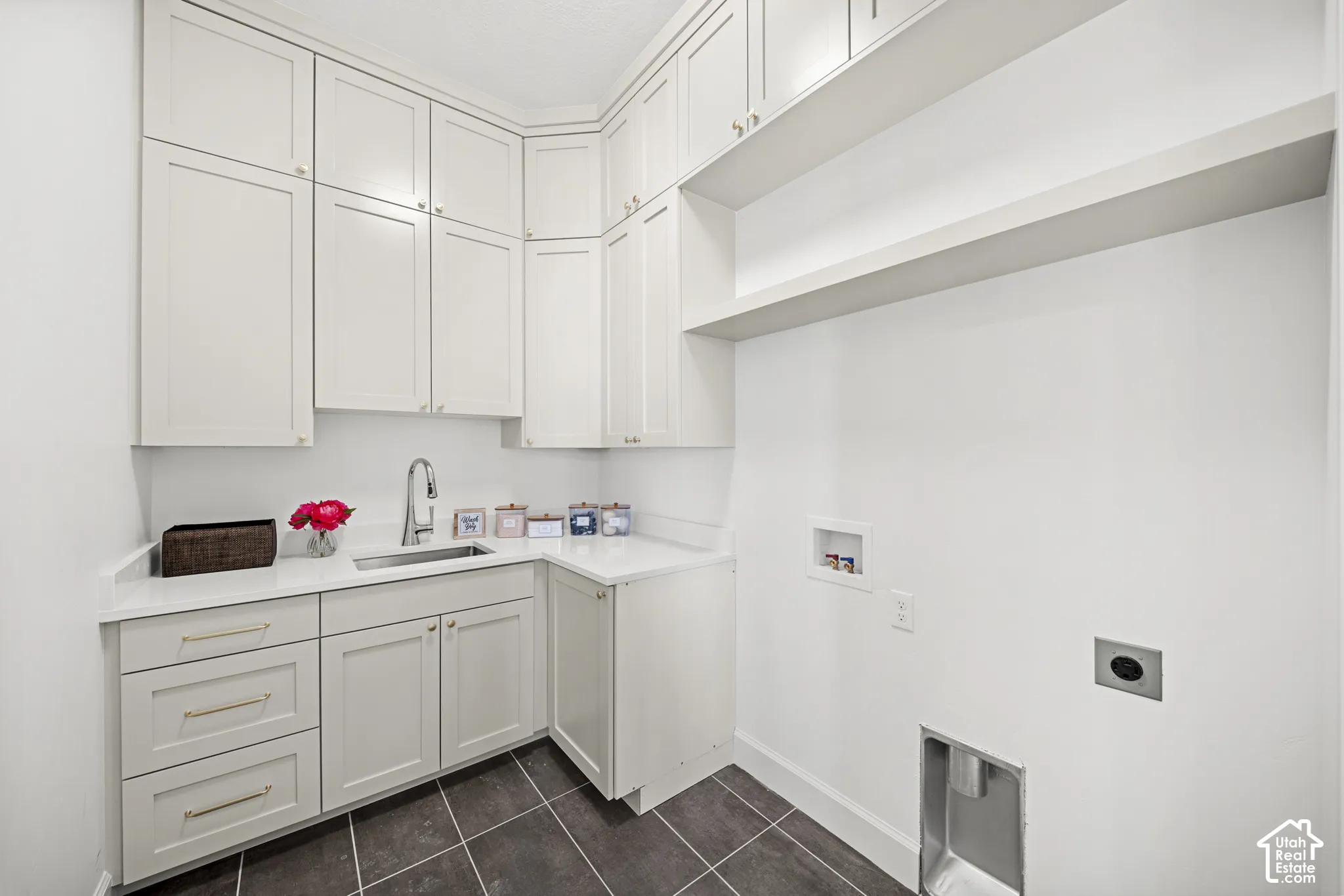 Integrated laundry area featuring extensive built-in cabinetry, solid surface countertops, an undermount sink with a gooseneck faucet, and dark tile flooring