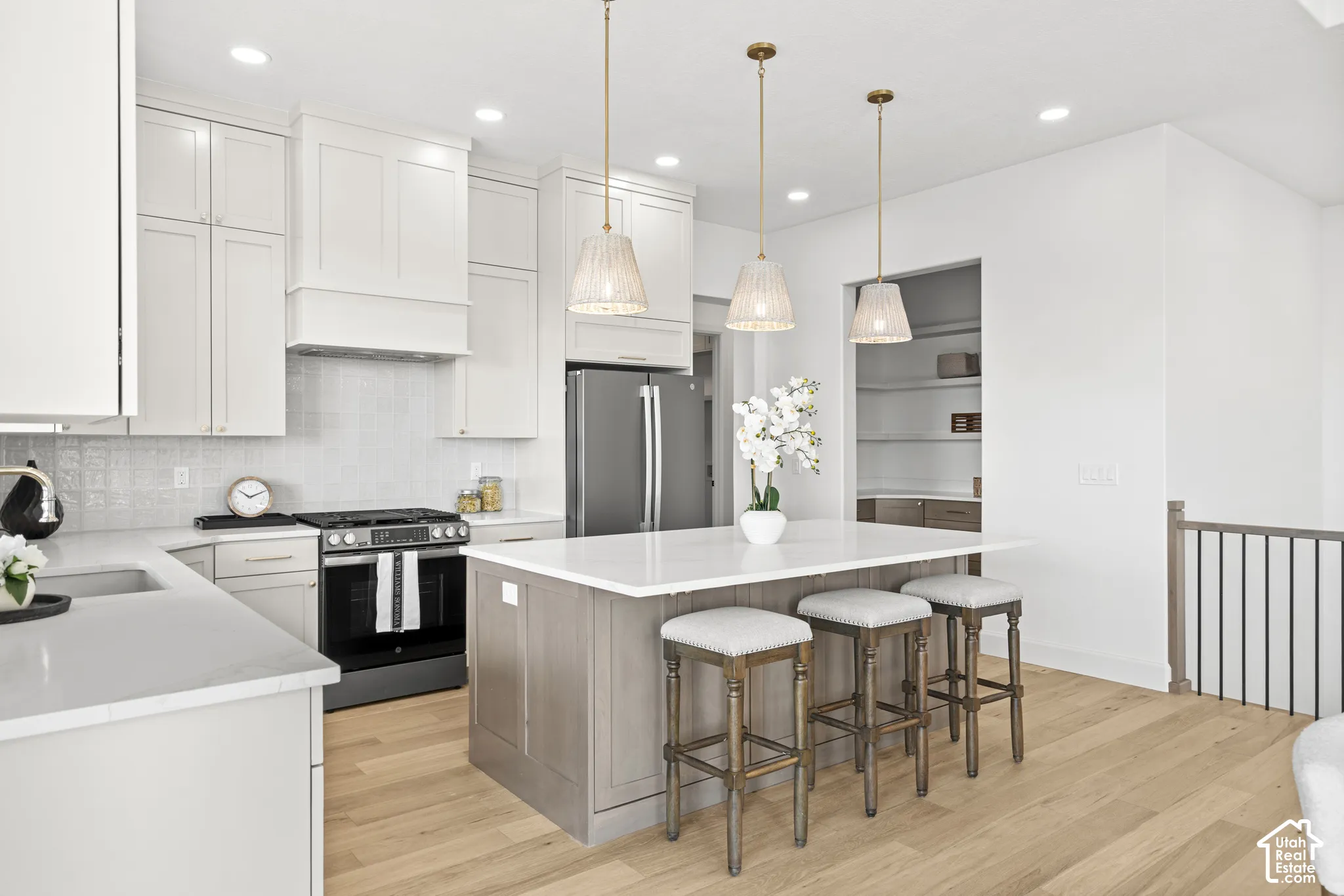 Modern kitchen with white cabinetry, stainless steel appliances, a center island with pendant lighting, light wood-finish flooring, and an integrated pantry with shelving