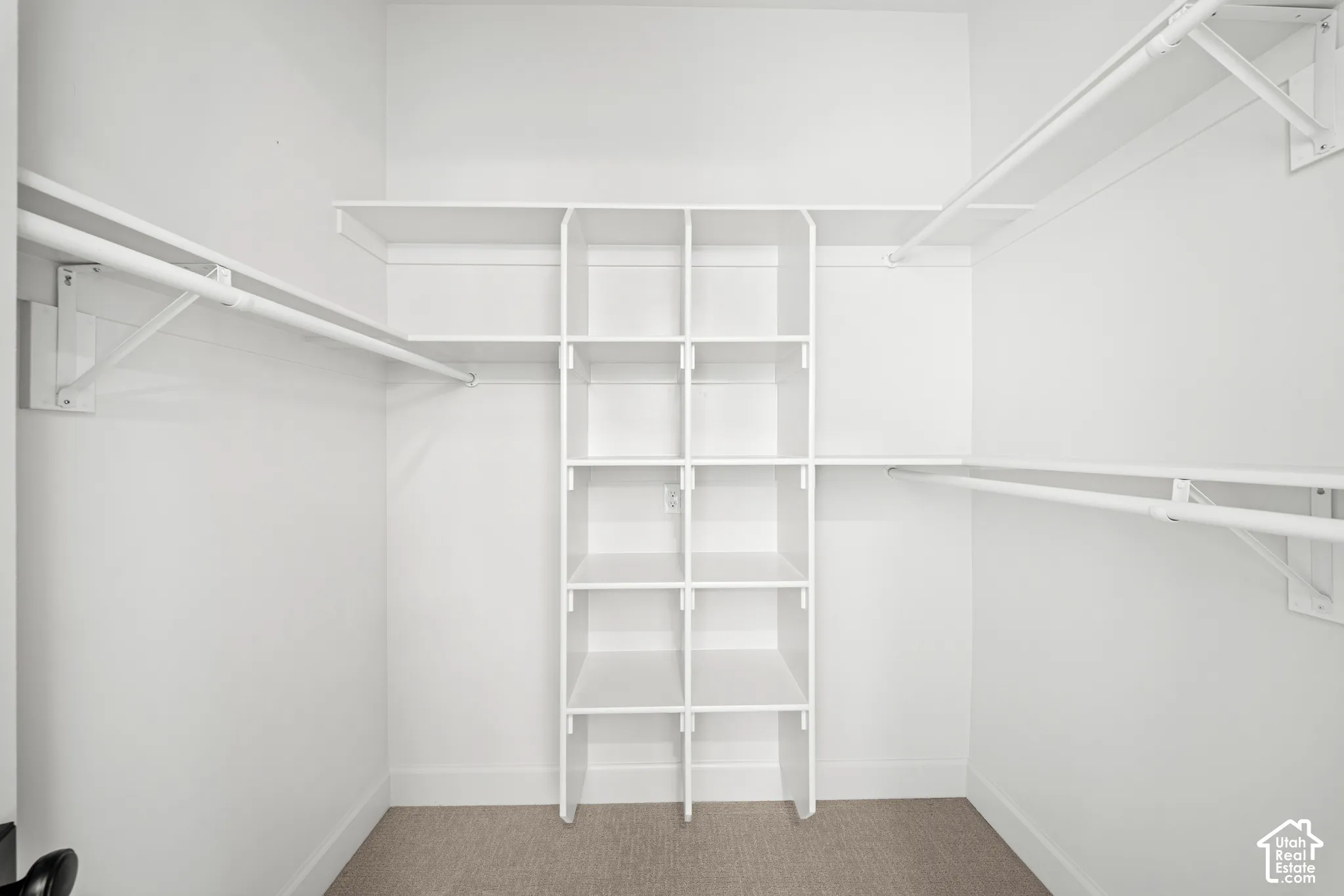 Walk-in closet with white shelving system, multiple hanging rods, built-in cubbies, and carpet flooring