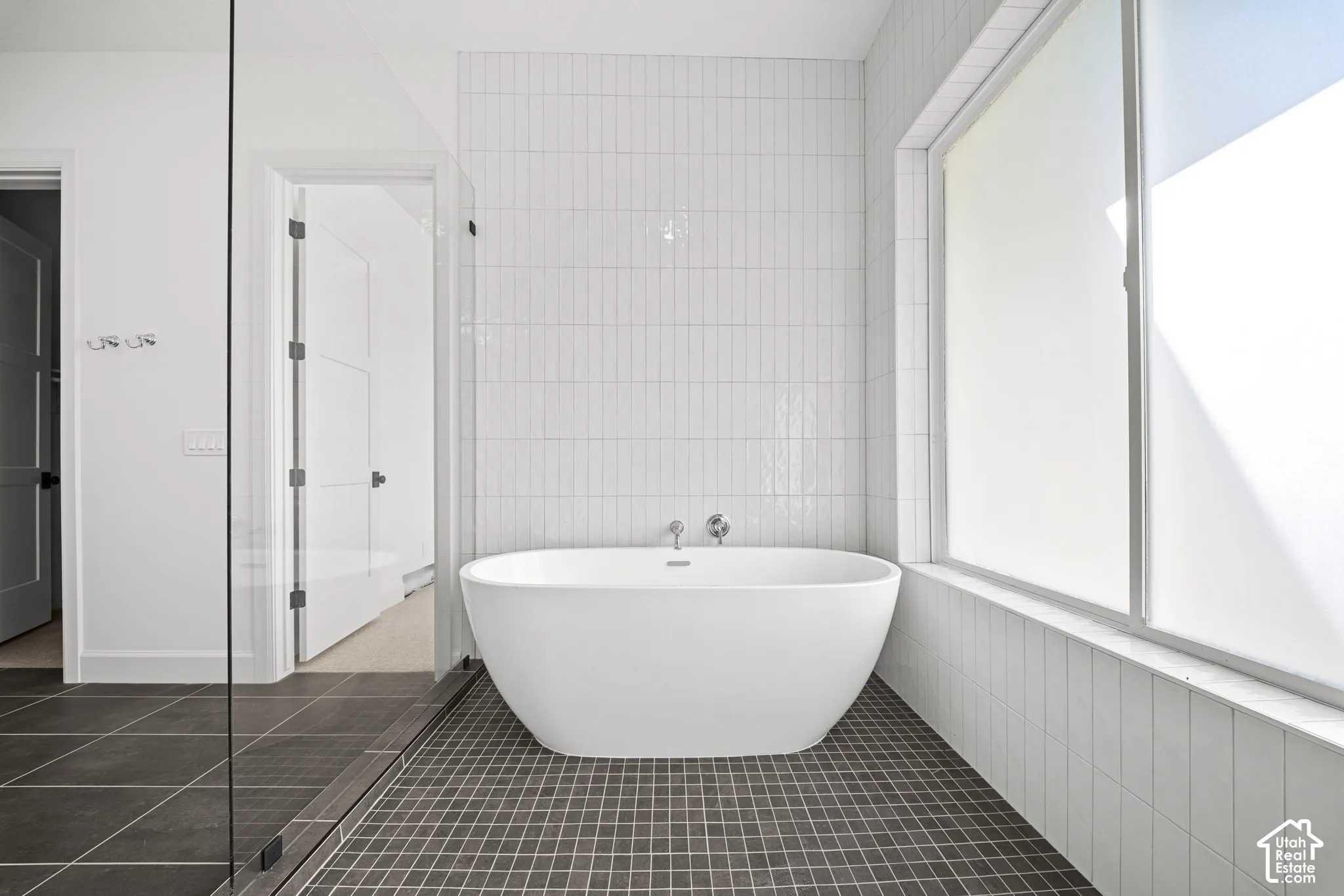 Freestanding soaking tub with wall-mounted fixtures, large privacy window, and tile flooring