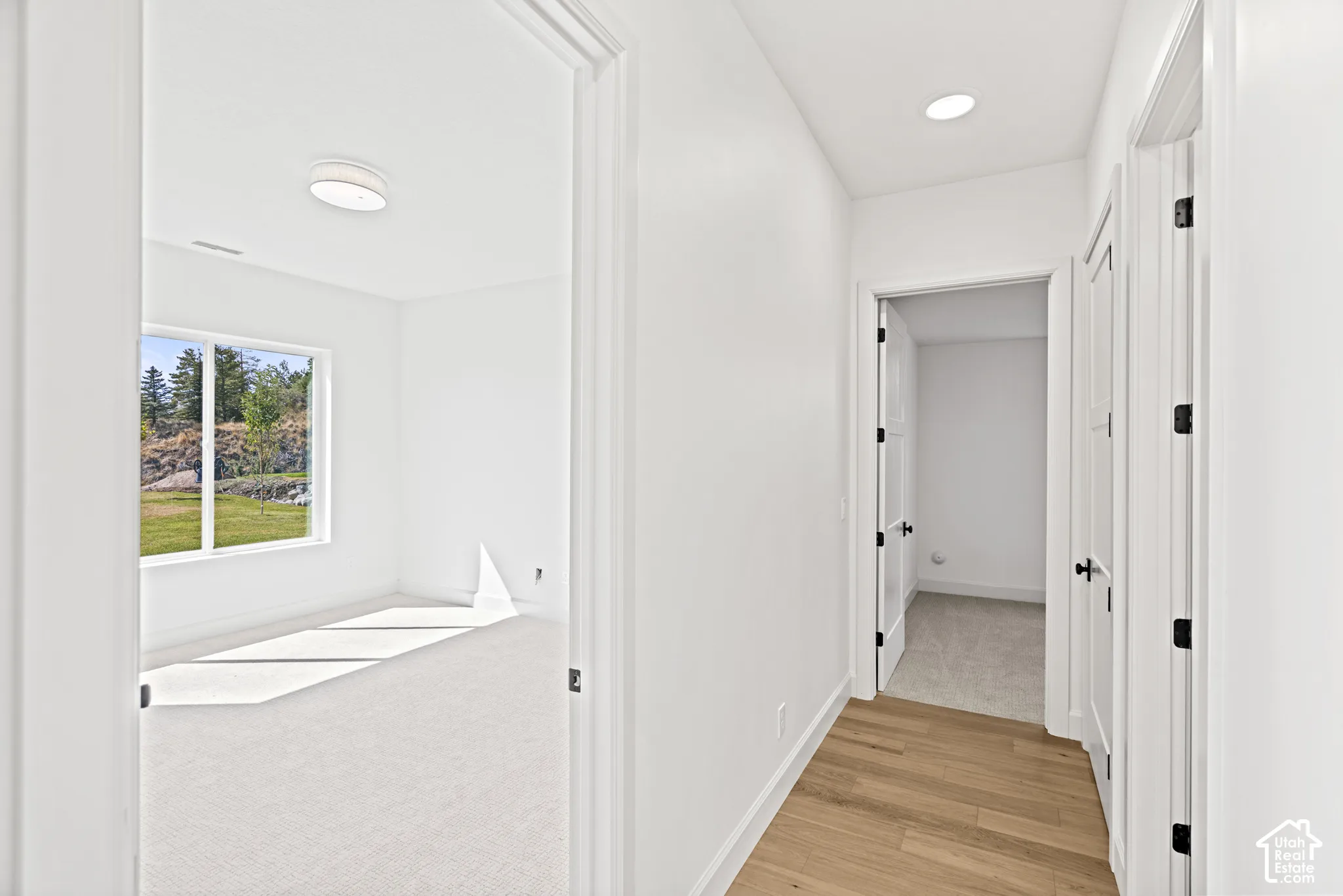Light wood-finish flooring, recessed lighting, white interior doors with dark hardware, and bright white walls