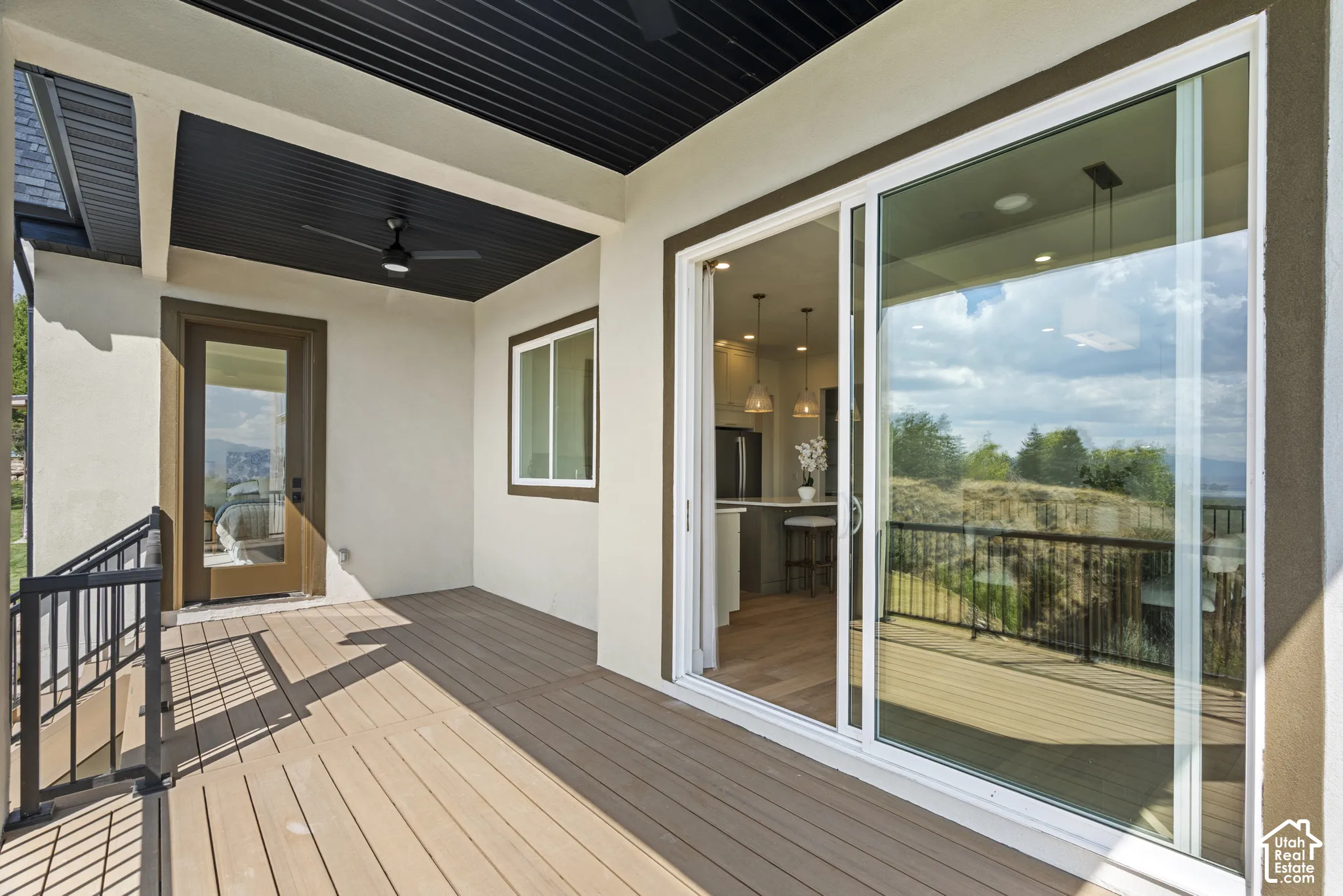 Spacious covered balcony with composite decking, black metal railings, a glass-panel door, and white frame sliding glass doors