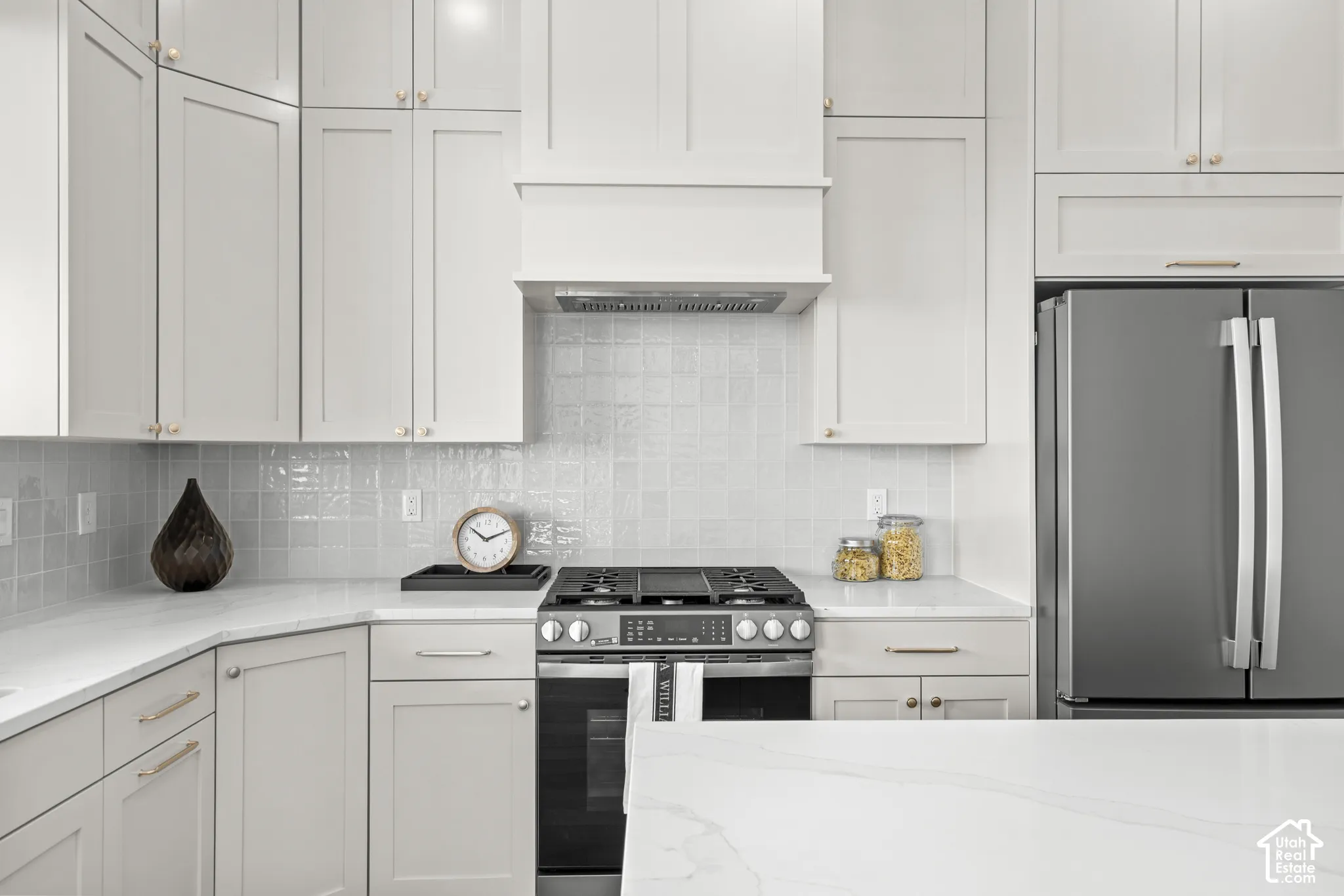 White shaker cabinetry and light countertops with an integrated stainless steel range and matching hood