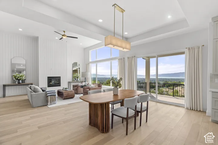 Spacious open-concept living area featuring light wood-finish flooring, a contemporary fireplace with white vertical paneling, and a white tray ceiling