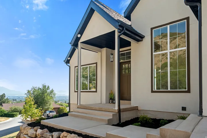 Stucco exterior with dark trim accents, covered entry porch, dark front door, large multi-pane windows, and concrete steps with integrated landscaping
