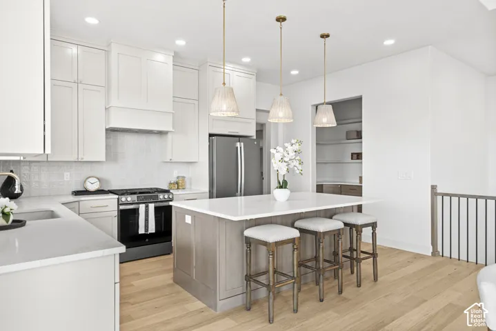 Modern kitchen with white cabinetry, stainless steel appliances, a center island with pendant lighting, light wood-finish flooring, and an integrated pantry with shelving