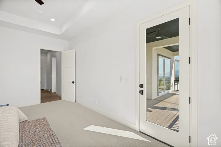 Recessed ceiling lighting, tray ceiling, carpeted flooring, white interior doors with black hardware, and a glass-paneled door leading to an outdoor deck
