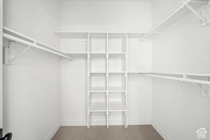 Walk-in closet with white shelving system, multiple hanging rods, built-in cubbies, and carpet flooring