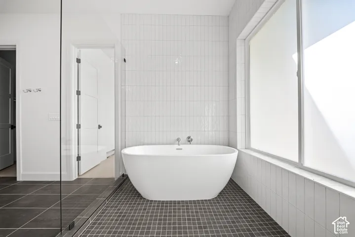 Freestanding soaking tub with wall-mounted fixtures, large privacy window, and tile flooring