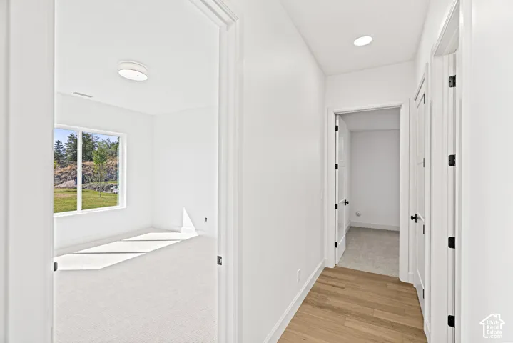 Light wood-finish flooring, recessed lighting, white interior doors with dark hardware, and bright white walls