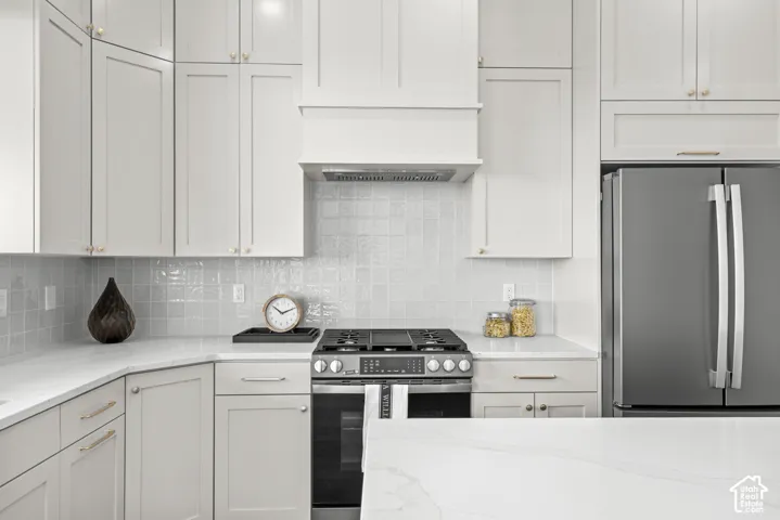 White shaker cabinetry and light countertops with an integrated stainless steel range and matching hood