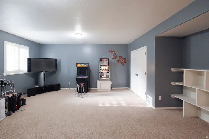Spacious recreation room with neutral carpet flooring, soft recessed lighting, and abundant natural light from large window