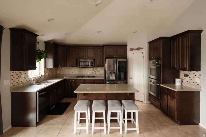 Kitchen featuring dark wood cabinetry, light-toned countertops, a mosaic tile backsplash, and stainless steel appliances