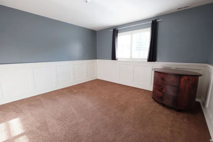 Wall paneling with a chair rail accent, window with blinds, and brown carpet flooring