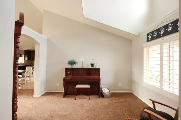 Vaulted ceiling, arched doorway, window with plantation shutters, broadloom carpet, crown molding