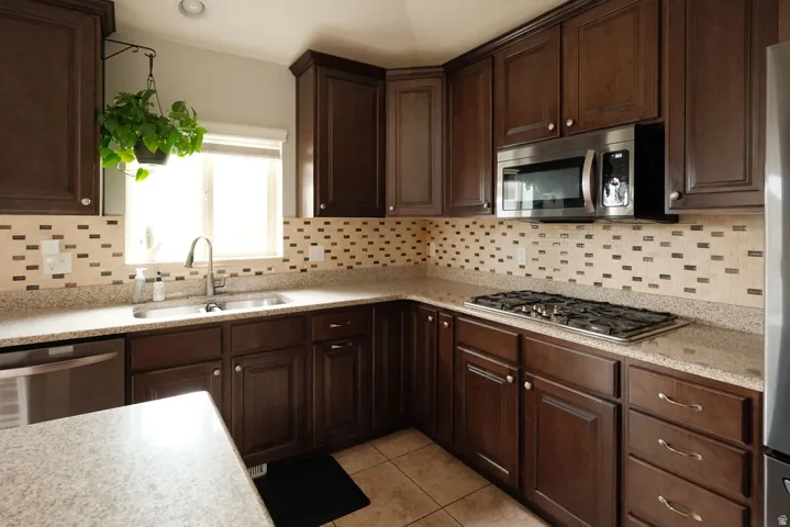 Kitchen featuring rich wood cabinetry, stainless steel appliances, speckled countertops, a tile backsplash, and a double-basin sink