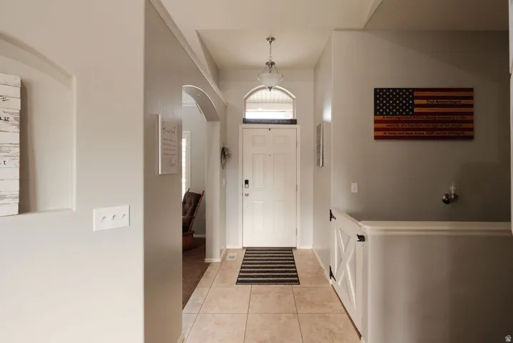 Welcoming foyer featuring tile flooring, arched doorway with transom window, white paneled wainscoting, and pendant lighting