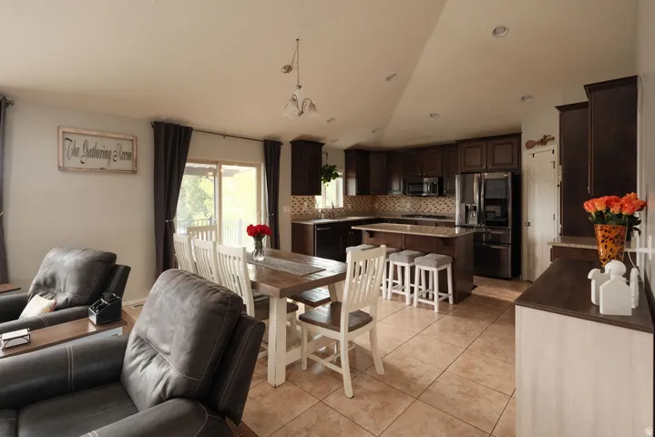 Open-concept layout featuring tile flooring, dark wood-finish cabinetry, a kitchen island with seating, a patterned tile backsplash, and stainless steel appliances