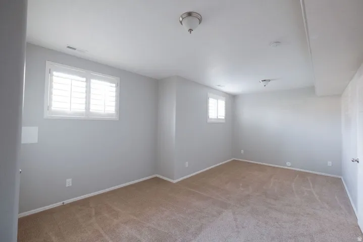 Neutral wall paint, carpeted flooring, two windows with plantation shutters, and flush mount lighting