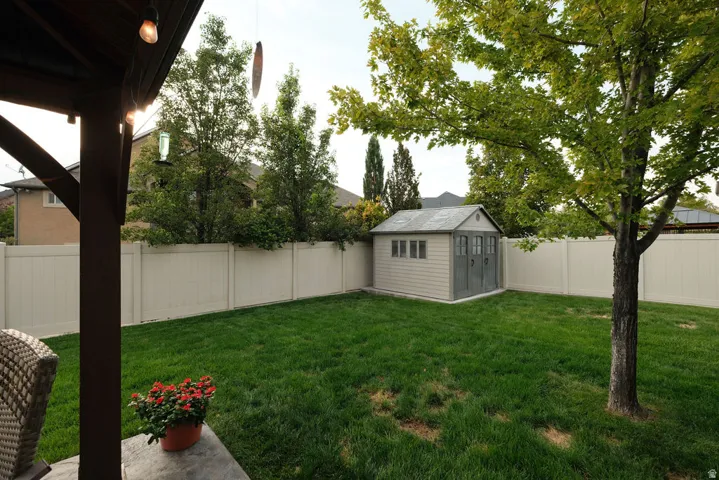 Gable roof storage shed, privacy fencing, mature tree, and green lawn