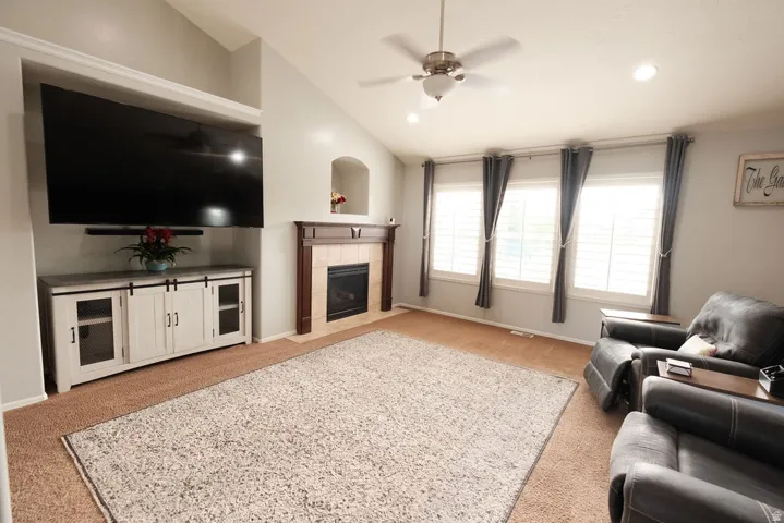 Vaulted ceiling with a ceiling fan, recessed lighting, and a fireplace with a wood mantle and tile surround