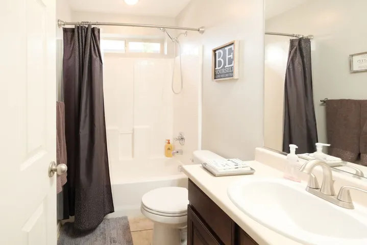 Full bathroom featuring a white tub and shower combination with a window, a white toilet, and a vanity with a drop-in sink and brushed nickel faucet