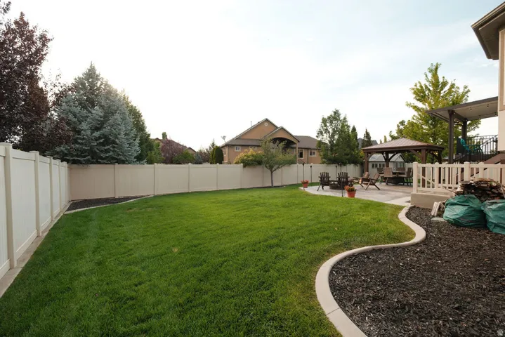 Expansive backyard featuring a large grass lawn, perimeter fencing, and a concrete patio with a detached gazebo