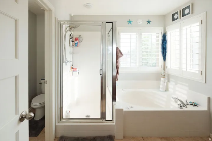 Built-in soaking tub, framed windows with plantation shutters, glass-enclosed shower, and a separate water closet