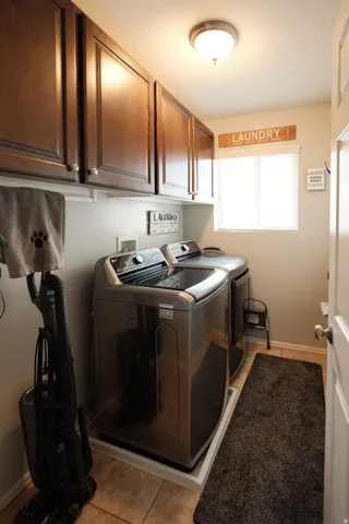 Dedicated laundry room featuring stacked washer and dryer units with metallic finishes, rich wood cabinetry with integrated storage, tile flooring, a window for natural light, and a "Laundry" designation sign above the cabinetry