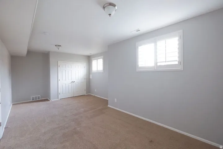 Carpeted room featuring a white bi-fold closet, two windows with white plantation shutters, and overhead flush-mount lighting fixtures