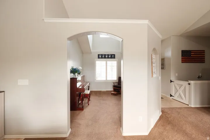 Archway entry with crown molding, vaulted ceiling, and interior shuttered window
