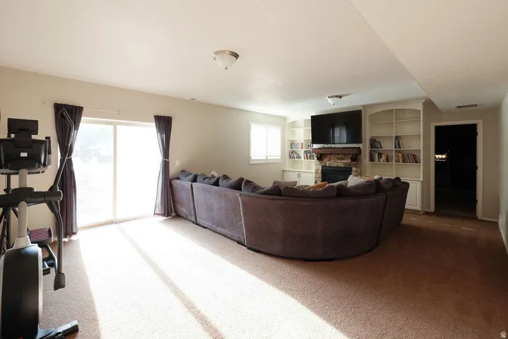 Spacious living area featuring a fireplace, built-in shelving, glass sliding doors, and neutral carpeting
