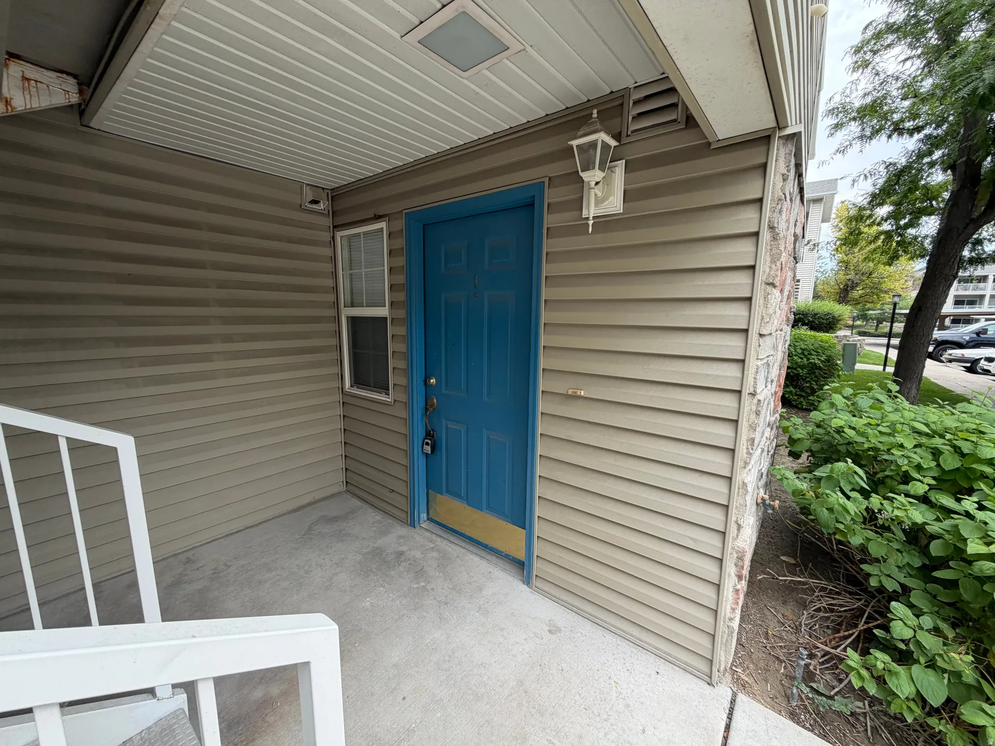 Entry with a blue door, horizontal siding, stone veneer accents, an exterior light fixture, and a white railing
