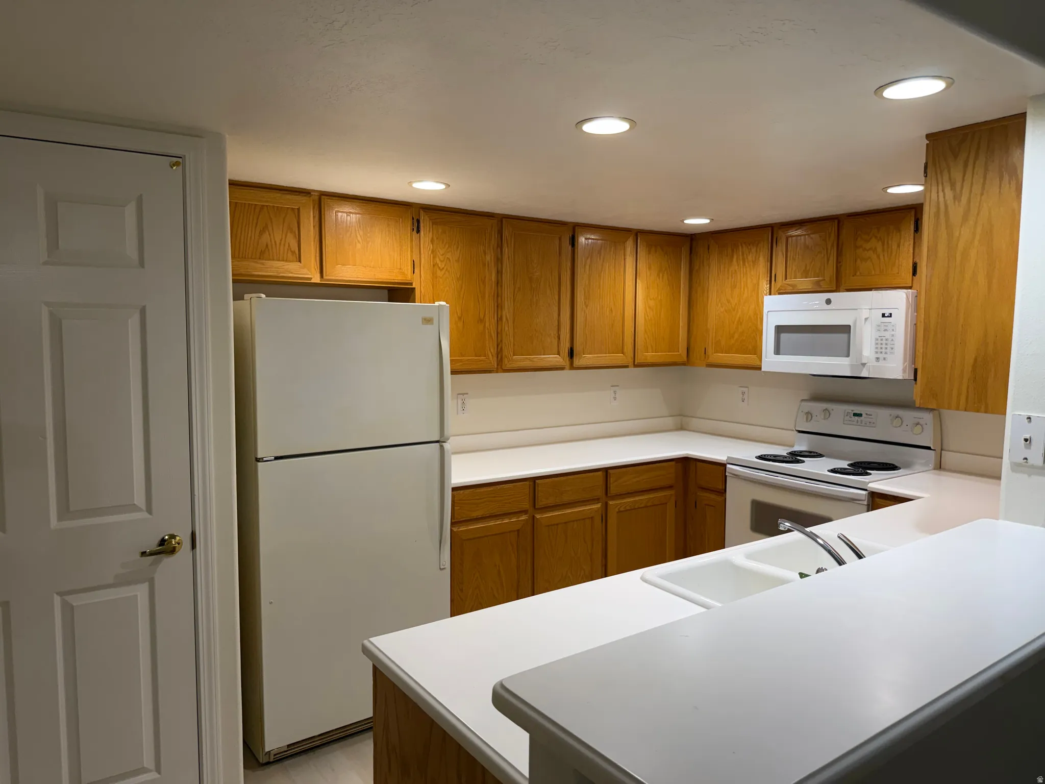 U-shaped kitchen with wood-finish cabinetry, white countertops, and a double basin sink