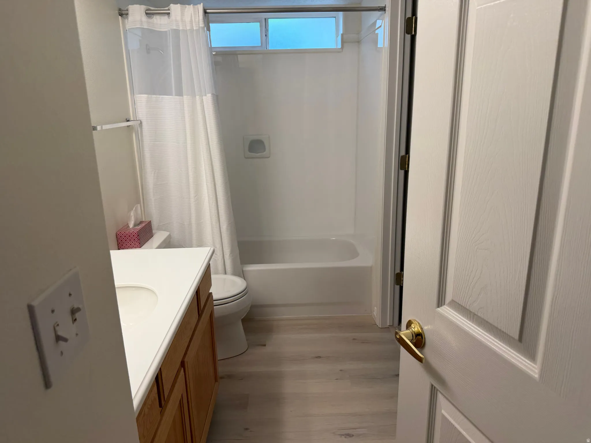 White vanity with an integrated sink, wood-finish cabinetry, and light wood-finish flooring