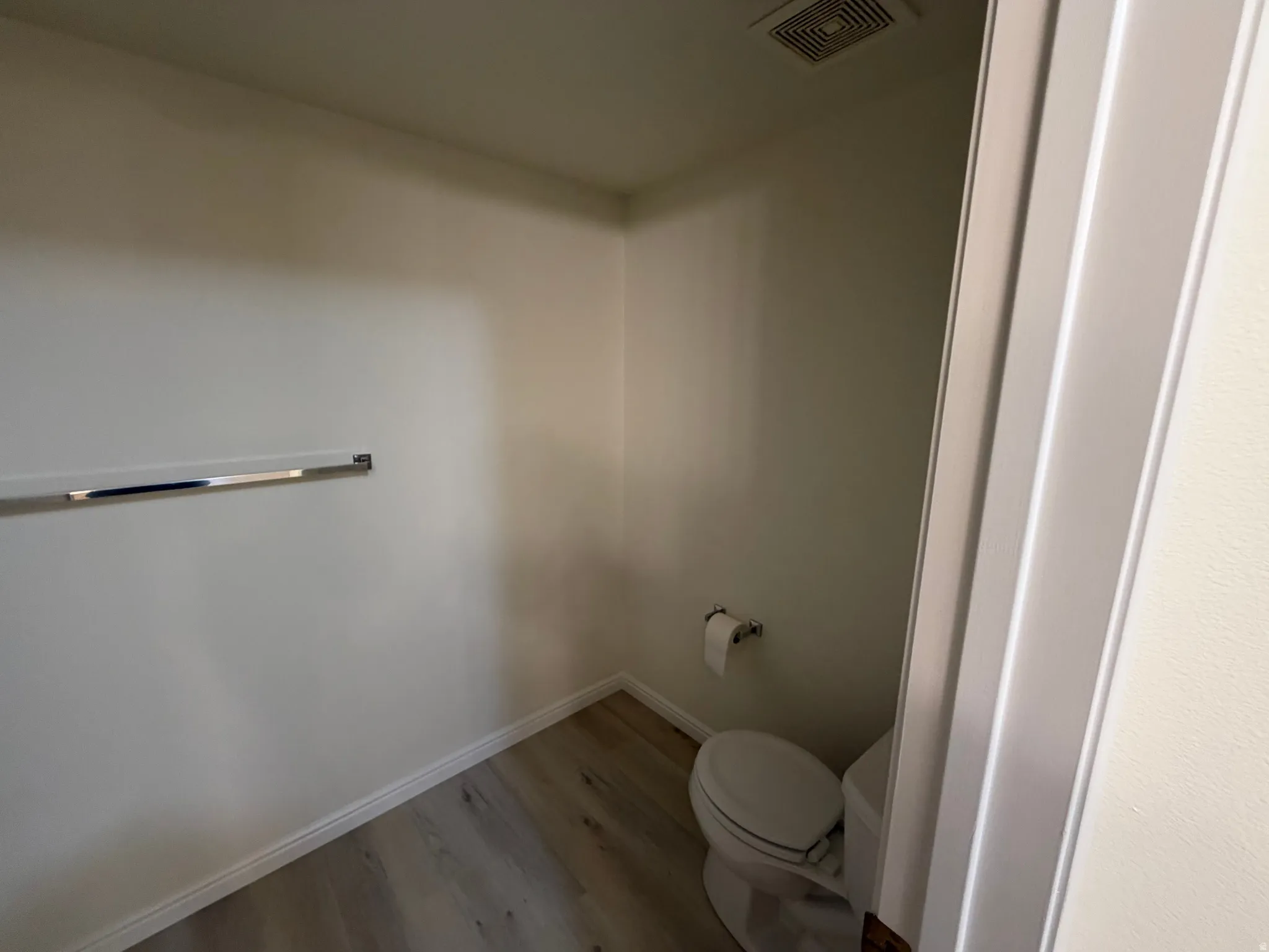 White walls with wood-finish flooring, a chrome towel bar, and a standard toilet