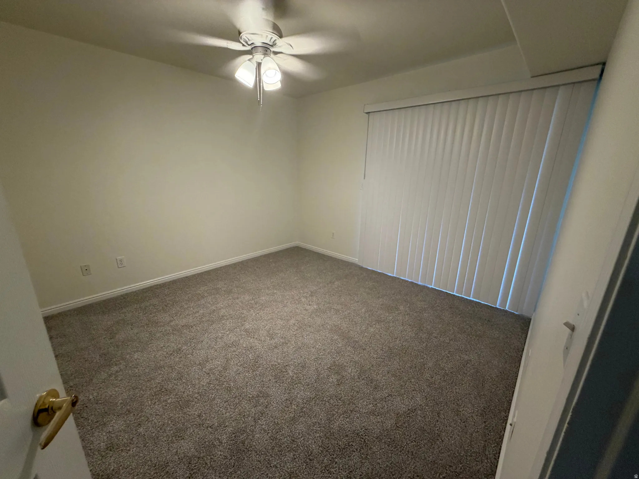 Plush gray carpeting, vertical blinds, ceiling fan with integrated lighting, and white trim