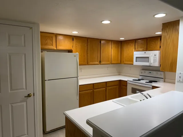 U-shaped kitchen with wood-finish cabinetry, white countertops, and a double basin sink
