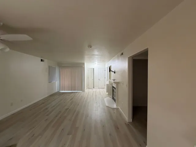 Spacious living area featuring light wood-finish flooring, a contemporary white fireplace, and a ceiling fan
