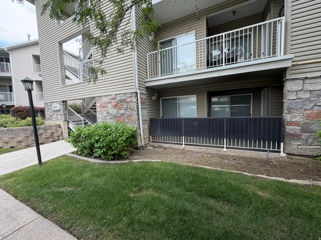 Exterior featuring horizontal siding, stone veneer accents, an upper-level balcony with metal railing, and ground-level patio with privacy screen