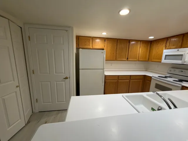 Kitchen with wood-finish cabinetry, white countertops, built-in white appliances, and a dual-basin sink